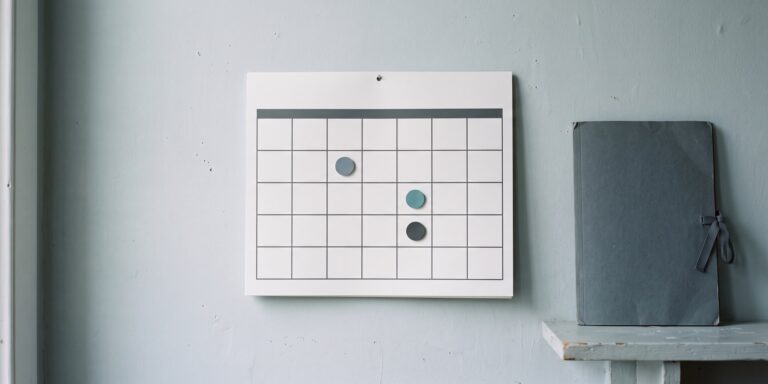 Wandkalender mit mehreren markierten Terminen, daneben ein aufgeschlagener Aktenordner als Sinnbild für gestaffelte Fristen