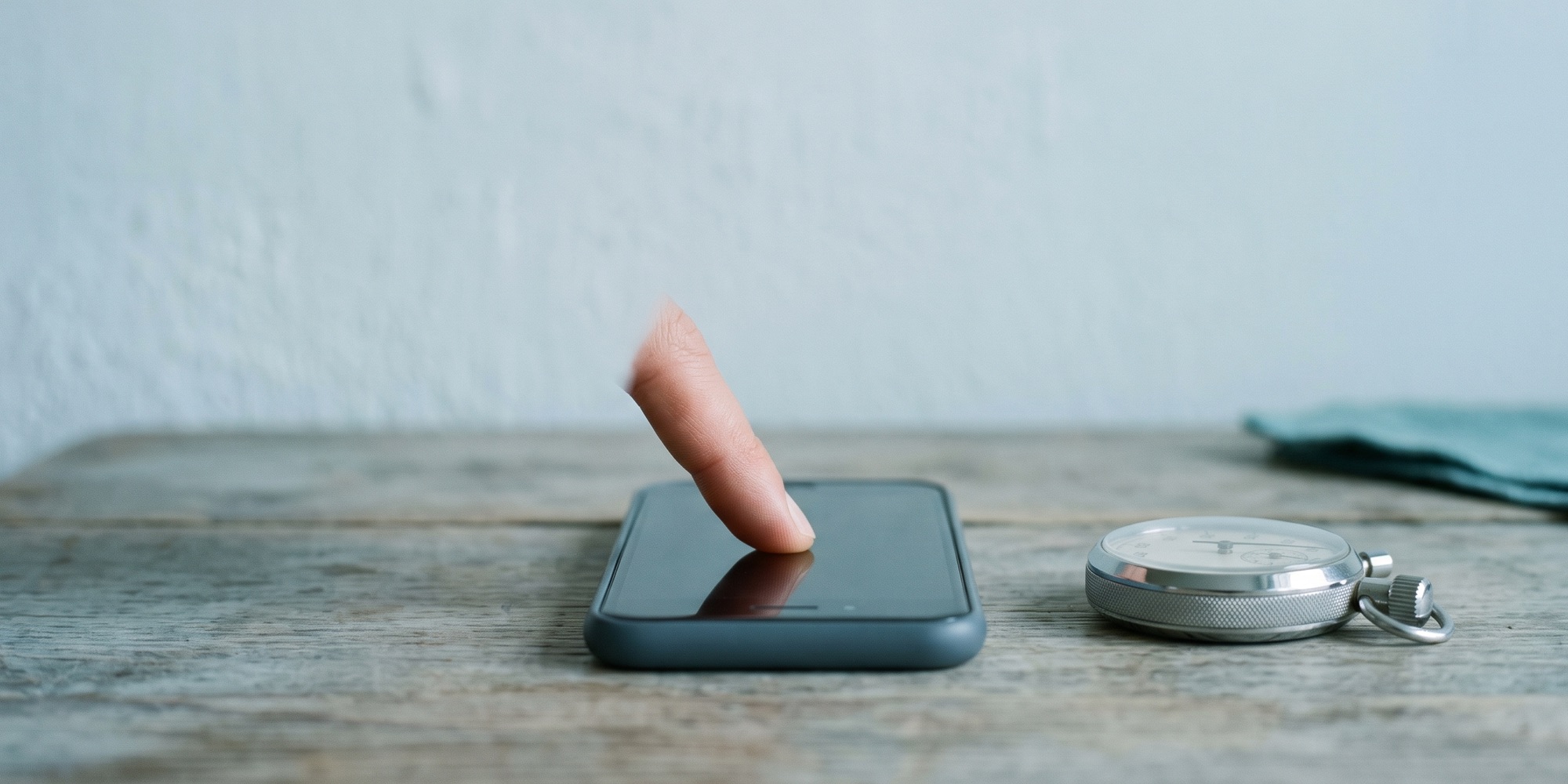 Finger tippt auf ein Smartphone-Display, daneben eine Stoppuhr als Sinnbild für die gemessene Reaktionszeit